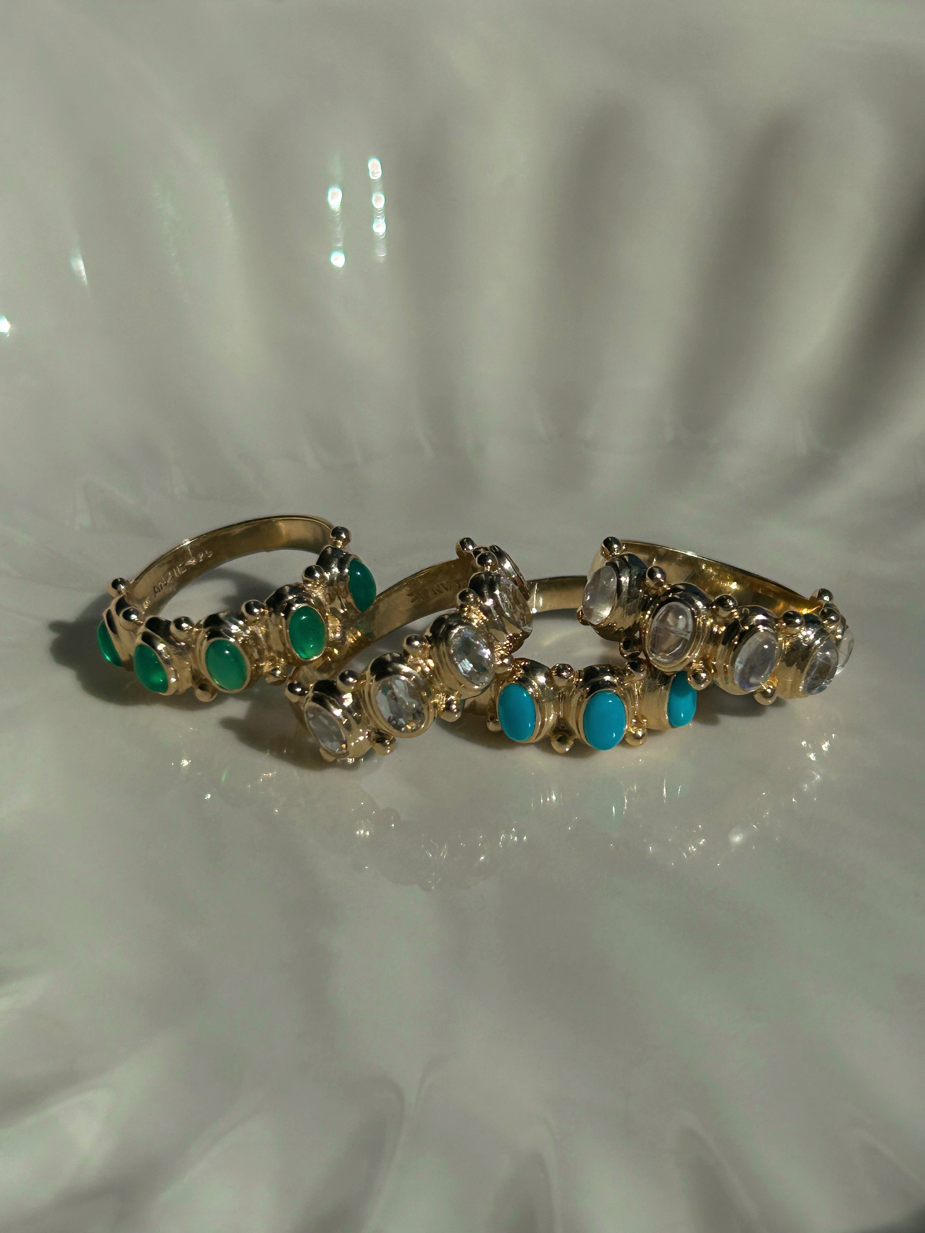 Two gold rings with gemstones on a white shell background