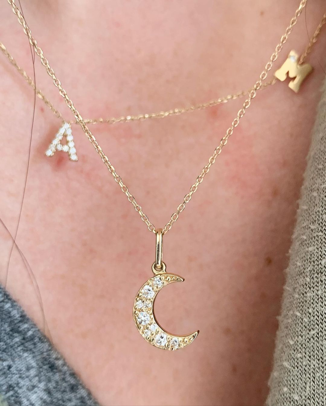Close up of woman wearing gold and diamond moon charm on a gold chain, layered with initial charm necklace