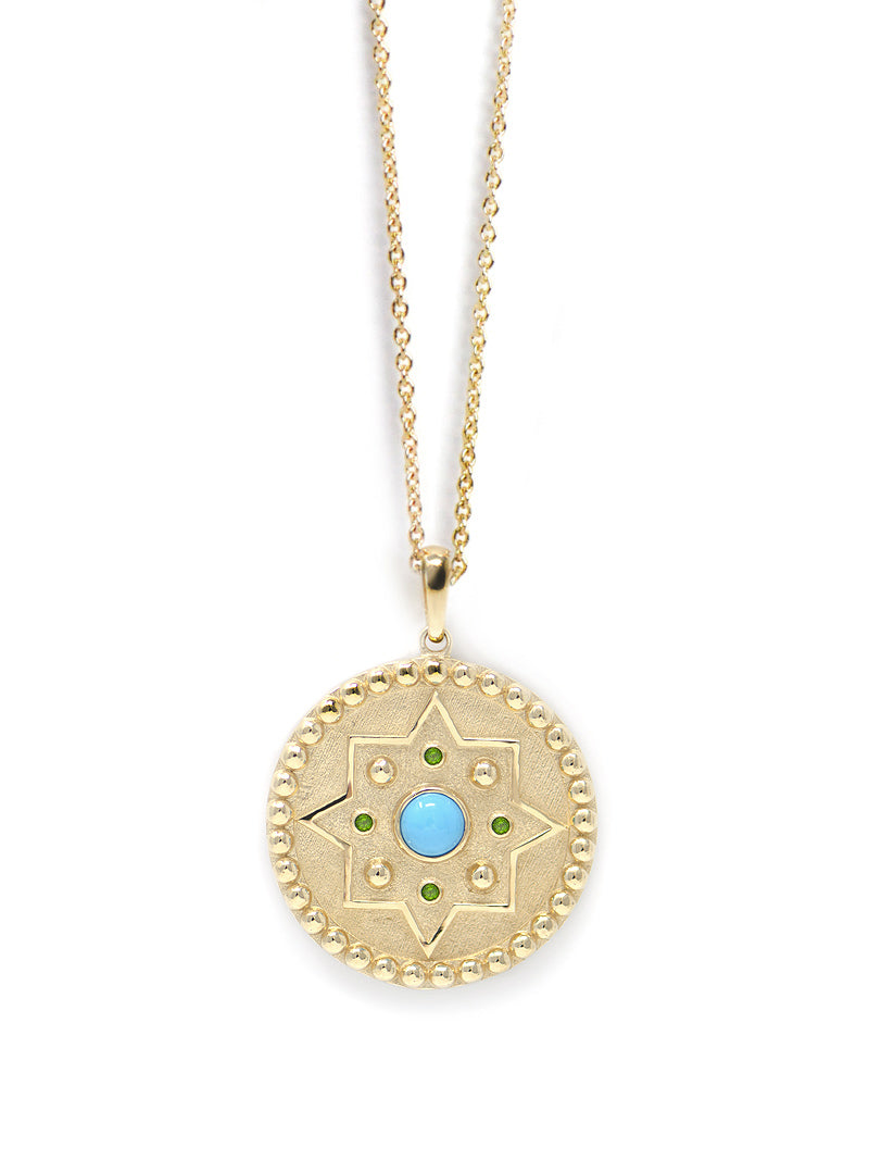 Gold star medallion with turquoise center stone and emerald accent stones on a thin gold chain